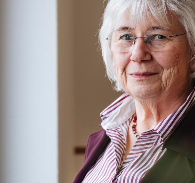 Ältere Dame, eine Beraterin, schaut milde in die Kamera und steht am Fenster